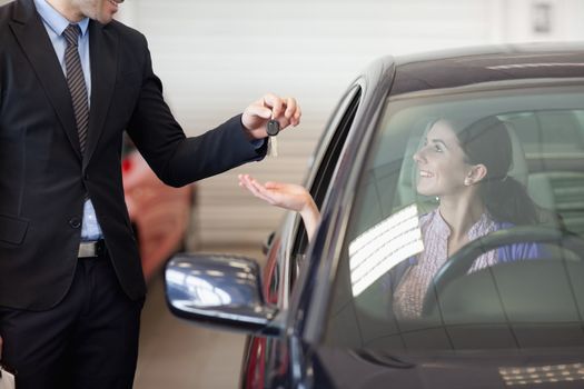 Smiling woman in a car taking keys in a car dealership