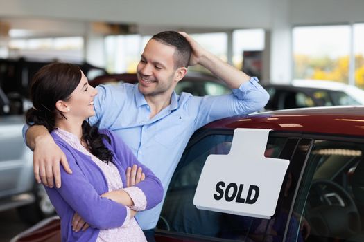 Smiling couple hugging next to a car in a car dealership