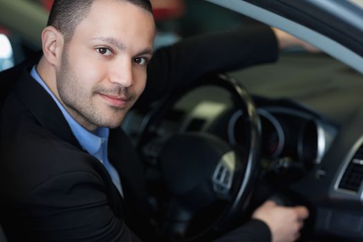 Man sitting on a car while turning on the engine in a car dealership