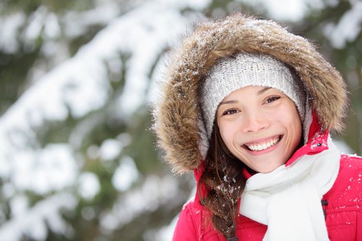 Winter woman portrait outdoors in snow forest. Smiling happy multiracial Asian / Caucasian female model blissful and content looking at camera on cold snowy winter day outside.