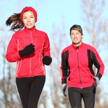 Healthy lifestyle winter running. Runner couple jogging in city park in warm winter sports clothing. Fit Asian woman fitness model and Caucasian man model.