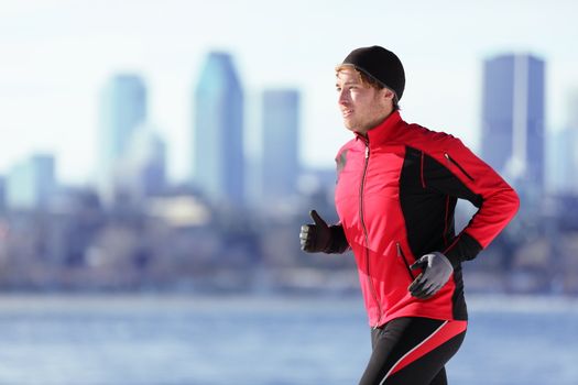 Athlete man running sport. Runner in winter jogging outdoors with city skyline in background. Male fitness model in Montreal, Canada.