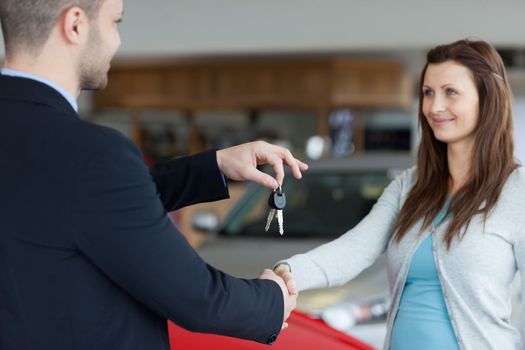 Salesman giving car keys while shaking hand of a woman in a garage