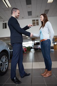 Salesman giving car keys while shaking hand of a client in a garage