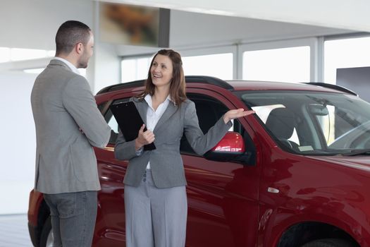 Businesswoman showing a car to a client in a dealership