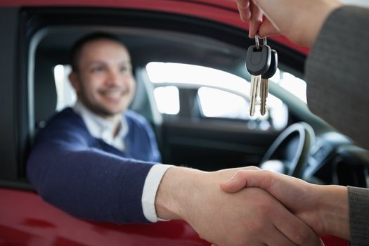 Woman giving car keys while shaking hand in a dealership