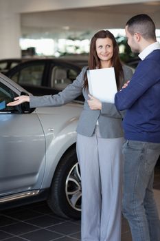 Woman showing a car to a client in a dealership