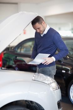 Man reading a file while looking at the engine in a garage