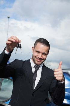 Man holding car keys while raising his thumb outdoors