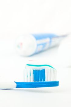 Tooth brush next to a tube of toothpaste against white background