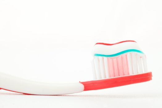 Toothpaste on a red toothbrush against white background