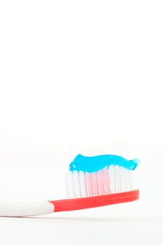 Blue toothpaste on a red toothbrush against white background