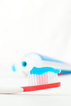 Red toothbrush next to a tube of toothpaste against white background