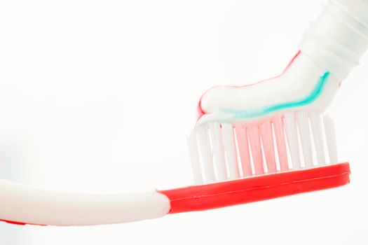 Red toothbrush with multicolour toothpaste against white background