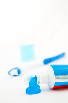 Blue toothbrush next to a tube of toothpaste against white background