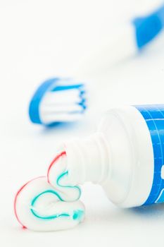 Blue toothpaste tube next to a toothbrush against white background