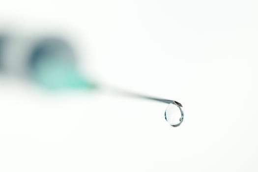 Close up of a drop outgoing of a syringe against white background