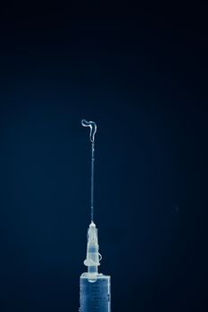 Syringe expelling liquid against a blue background