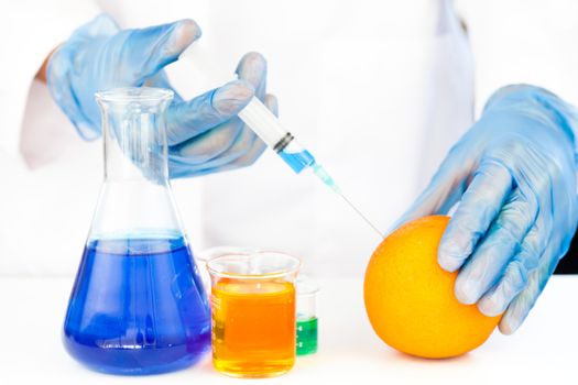 Chemist injecting product in an orange against a white background