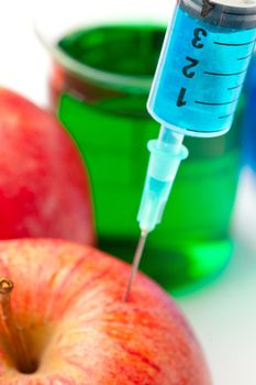 Close up of a syringe injecting liquid into an apple against a white background