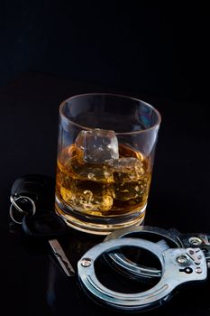 Whiskey on the rocks with car key and handcuff against a black background
