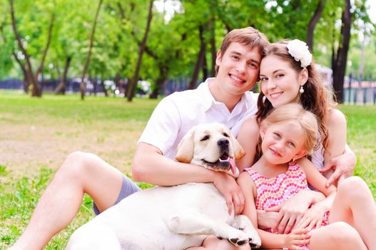 Happy young family with Labrador is resting in the park