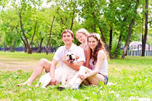 Happy young family with Labrador is resting in the park