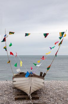 Image of a boat decorated with colorful flags located on a rocky beach in Normandy in north of France.