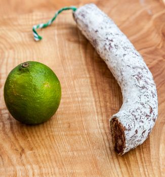 A piece of dried French sausage and a lime on a wooden board.