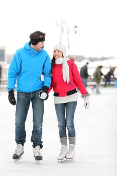 Romantic young couple in warm winter clothing holding hands and smiling at each other while ice skating.