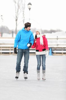 Young couple holding hands iceskating outdoors on a frozen lake or open-air rink against a snowy winter landscape