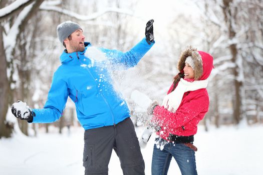 Carefree happy young couple having fun together in snow in winter woodland throwing snowballs at each other during a mock fight