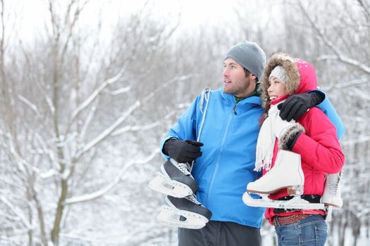 Young interracial couple in winter carrying ice skates standing close together looking out over a snowy winter landscape with copyspace. Asian woman, Caucasian man.