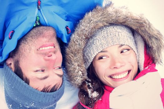 Happy winter couple. Cropped view of the faces of a joyful young interracial Asian / Caucasian couple lying on their backs in snow with their heads close together.