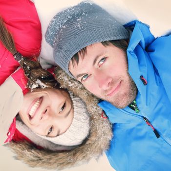 Winter couple happy. Overhead view of the heads of happy attractive interracial Asian / Caucasian couple lying in snow in warm winter clothing