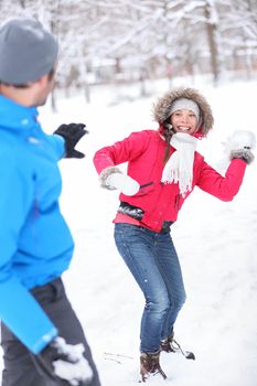 Young couple playing in the snow in snowball filght with a vivacious smiling Asian girl taking aim at her husband with a snowball