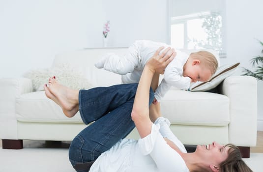 Mother lying on back playing with a baby in living room