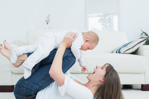 Mother lying playing with a baby in living room