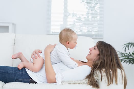 Mother lying on a sofa holding a baby on her chest in living room