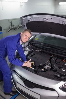 Mechanic leaning on a car while looking at camera in a garage