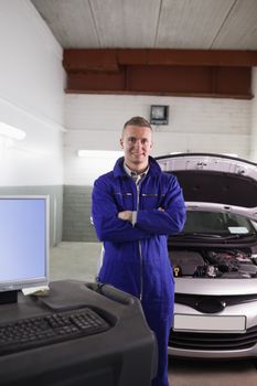 Mechanic next to a car and a computer with arms crossed in a garage
