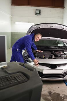 Smiling mechanic leaning on a car next to a computer in a garage