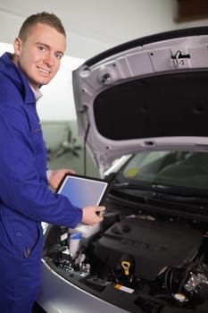 Smiling mechanic testing an engine with a tablet computer in a garage