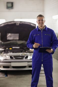 Mechanic holding a clipboard next to a car in a garage