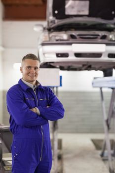 Smiling mechanic looking at camera next to a car in a garage