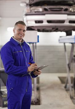 Smiling mechanic writing on a clipboard in a garage