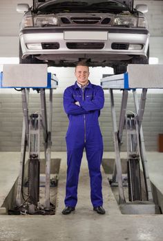 Mechanic standing with arms crossed below a car in a garage