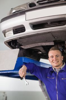 Smiling mechanic holding a spanner below a car in a garage