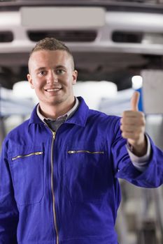 Mechanic standing with thumb up next to a car in a garage