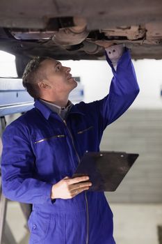 Mechanic looking at the below of a car while holding a clipboard in a garage
